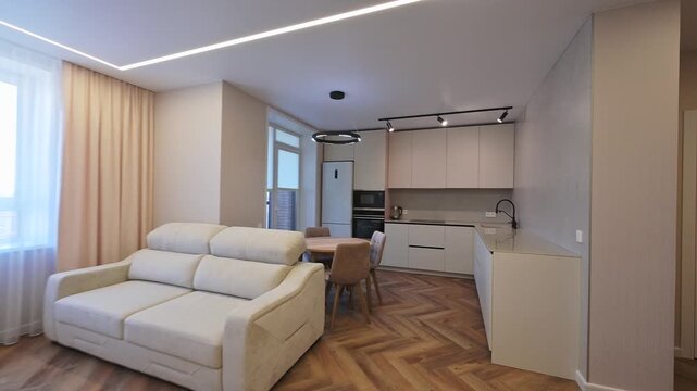 Modern apartment interior with a cozy sofa, elegant curtains, and a functional kitchen area. Stylish herringbone wood floor.