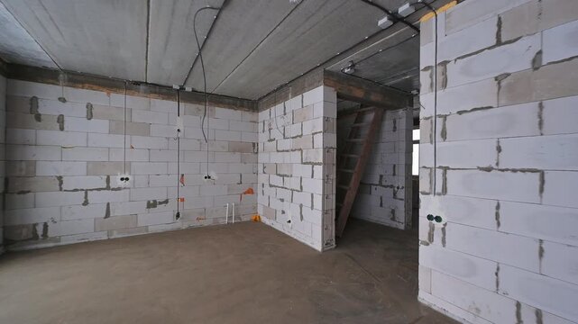 An unfinished room with cinder block walls, a concrete floor, and exposed wiring. A ladder is visible in the background.