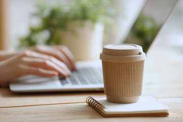Reusable eco coffee cup on notebook with laptop in sustainable home office environment