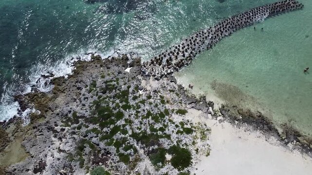 Drone aerial view of ocean shoreline with wave breakers visible under clear turquoise water transparent surface reveals rocks and marine patterns peaceful seascape from above