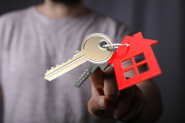 Close up of a hand holding house keys with a red house charm. Symbol of homeownership, real estate,...