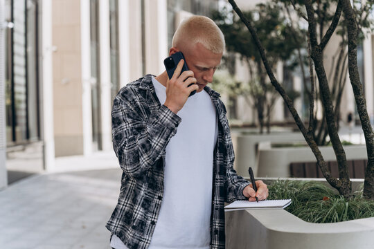 Young man with notepad and phone in urban setting