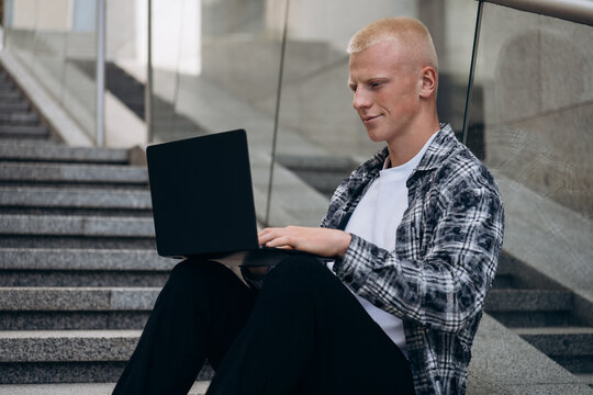 Young man with albino appearance using laptop on stairs