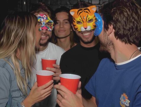 A lively group of friends wearing fun animal masks laugh and pose with red cups at a party