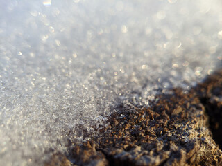 Glittering white snow crystals meeting the dark, rough surface of frozen, weathered wood