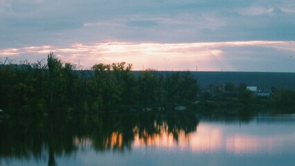 Obraz premium Evening light breaking through clouds over calm reflective lake