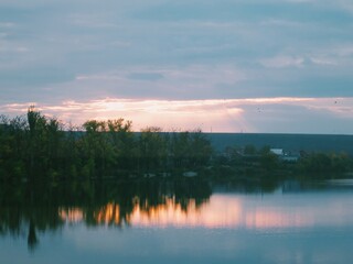 Tranquil riverside village and trees mirrored at pastel sunset