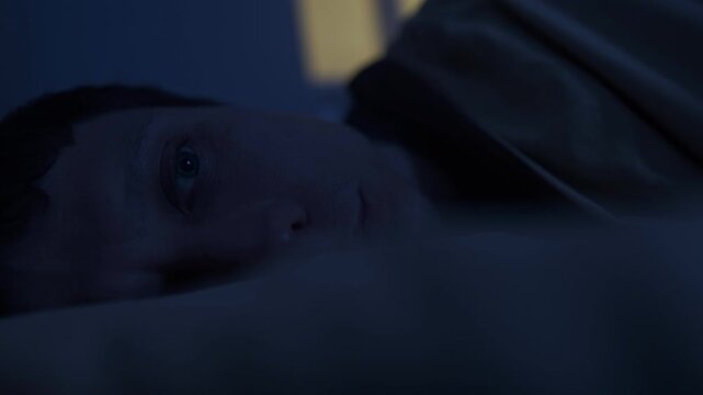 Man lying in bed suffering from insomnia night, sleepless bed and sleep deprivation, awake at midnight, close-up