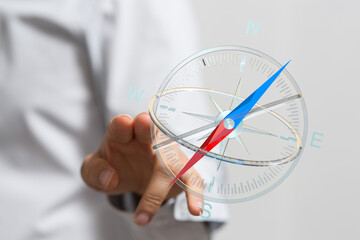 Fototapeta premium Close-up of a hand pointing at a compass, representing direction, guidance, and navigation. Concept of choices, travel, and exploration.