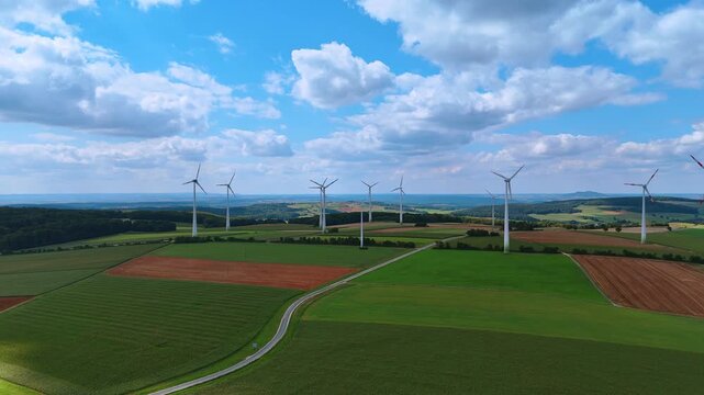Flight above the beautiful green fields crossed by the highway. Windfarm produces sustainable energy in the countryside.