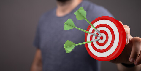 Close-up of a person's hand holding a dartboard with three darts hitting the center. Represents success, focus, and achievement in business and