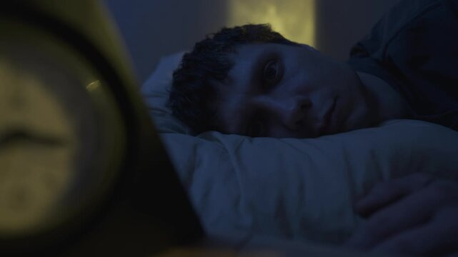 Man in bed staring into space, close-up. Sleepless night concept, mental stress and wakefulness in dark bedroom.
