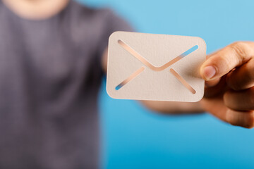 Close-up of a person's hand holding a paper email icon. Ideal for concepts like communication, digital message, and online correspondence.