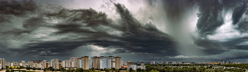 A dramatic panoramic view of the Darnytskyi district on the left bank of Kyiv, Ukraine. Massive, dark summer storm clouds and a rain shaft gather over the city's modern apartment buildings.