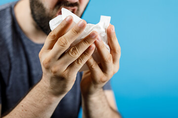 Close-up of a man using a tissue to blow his nose, depicting illness, allergies or a cold. The image represents common ailments and personal car