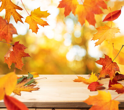 Wooden table with red-yellow leaves and blurred autumn background. Autumn background.