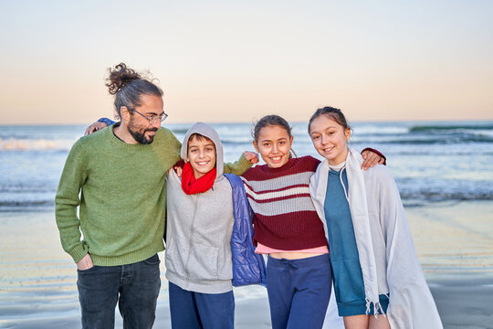 A man and three children stand together on a beach at sunset