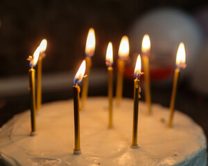 Close-up of a birthday cake with white frosting and several lit golden candles, casting a warm glow, capturing the festive and intimate atmosphere of a celebration