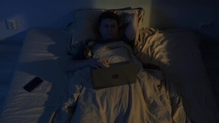 Man lying awake at night using laptop in bed, blue screen light causing insomnia