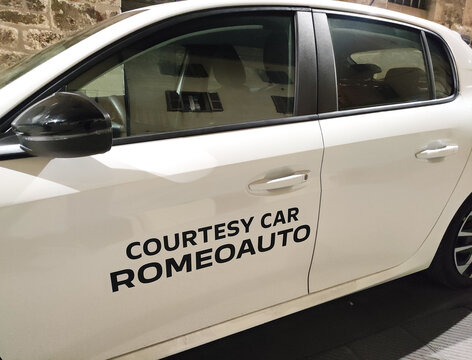Rome, Italy - October 27, 2025: White courtesy car from Romeauto parked on street, showcasing sleek design and modern features, ideal for rental service imagery