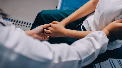 Fototapeta premium Doctor giving hope. Close up shot of young female physician leaning forward to smiling elderly lady patient holding her hand in palms. Woman caretaker in white coat supporting encouraging old person