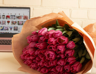 Online Flower Shopping Concept Beautiful Fresh Flower Bouquet in Focus with Blurred Laptop Screen Showing Online Flower Search, Symbolizing E-Commerce and Internet Flower Delivery Service. red tulips