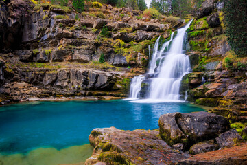 A beautiful waterfall in Ordesa National Park cascades over mossy rocks into a crystal-clear turquoise pool, surrounded by rugged cliffs and lush vegetation in a serene mountain landscape © david