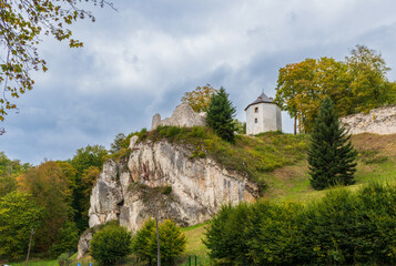 Obraz premium Medieval castle remains sit atop a limestone hill under cloudy sky. The mix of stone walls, trees, and natural slope evokes history, strength, and mystery of ancient architecture.