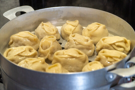 Delicious Manty, posture, khinkali is prepared in a special pot - mantoverde. Dishes of Asian, Buryat, Georgian cuisine. Aluminum steamer for cooking mantas on a stove in a home kitchen. Meat food.