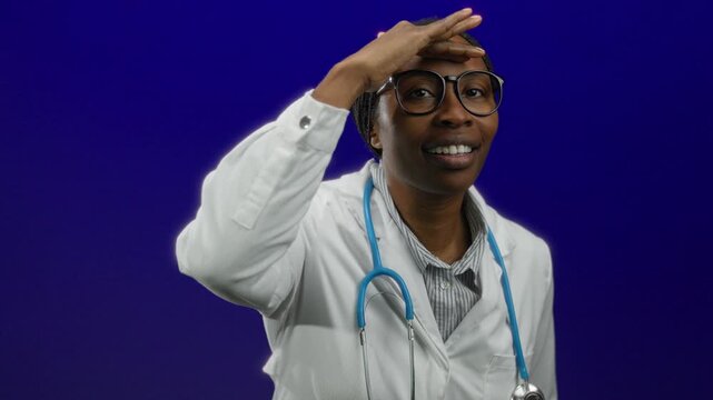 Woman doctor smiling against blue background with stethoscope wearing white coat and glasses featuring isolated professional healthcare provider adult black female medical.