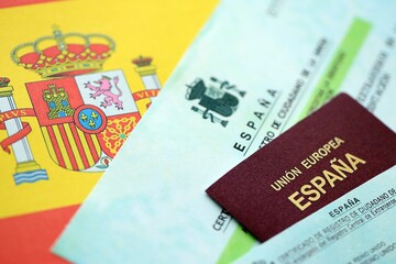 Spanish passport lies on citizenship or naturalization documents on flag of Spain close up