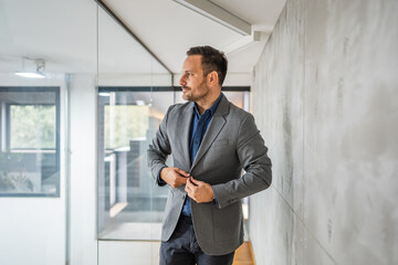 Confident businessman adjusting suit jacket in office