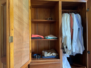 an open wardrobe with a belt on the top shelf and another on the bottom shelf, along with folded clothes and shirts hanging on hangers in the same wardrobe