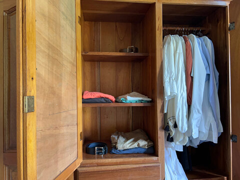 an open wardrobe with a belt on the top shelf and another on the bottom shelf, along with folded clothes and shirts hanging on hangers in the same wardrobe