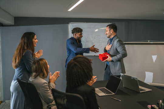 Office colleagues celebrating employee receiving gift at meeting