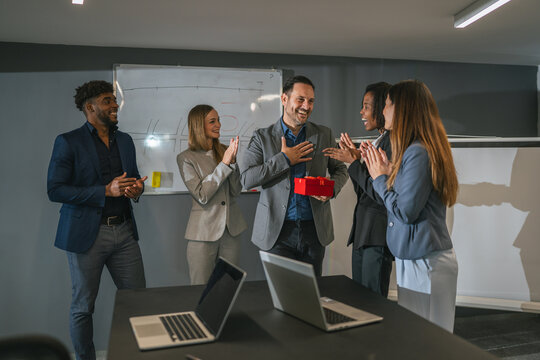 Diverse business team celebrating colleague's recognition with gift during office party