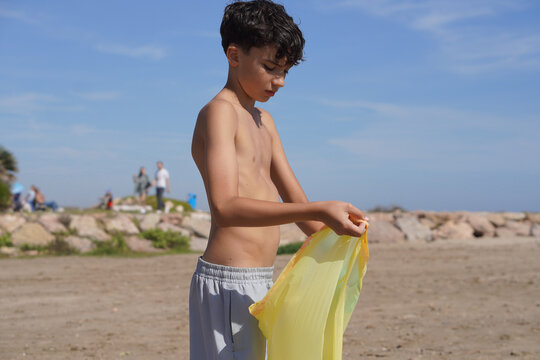 preteen volunteer, taking a walk on the beach in summer, collecting plastic from the seashore.