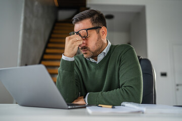 Stressed man experiencing headache while working on laptop