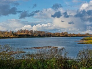 Tranquil autumn river scene with distant houses and a bright, cloudy sky