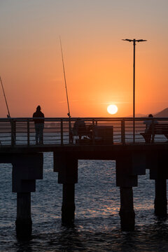 Santos city, Brazil. Colorful sunset at Fishermen's Deck. Silhouettes of people fishing and enjoying the view.