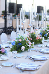 Wedding dinner table decoration with fresh colorful flowers, plates and candles. Long wedding table with crystal chairs. Celebration details, outdoor wedding in garden during summer