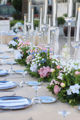 Wedding dinner table decoration with fresh colorful flowers, plates and candles. Long wedding table with crystal chairs. Celebration details, outdoor wedding in garden during summer