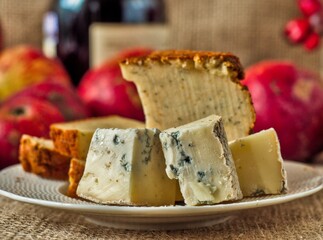Blue cheese gorgonzola and pepper jack cheese - A plate featuring slices of gourmet cheese with a wine bottle and apples blurred in the background