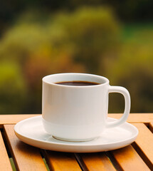 A white coffee cup with a brown liquid in it sits on a wooden table