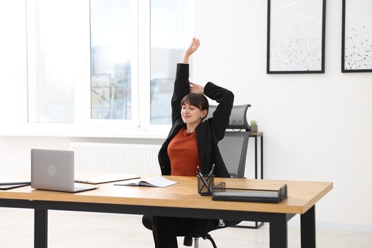 Young businesswoman stretching her arm at table in office