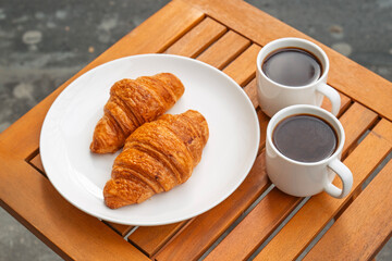 A plate of croissants and two cups of coffee sit on a wooden table