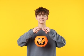 Halloween celebration. Boy with pumpkin bucket on orange background