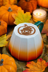 A cup of coffee latte topped with Halloween ghost pumpkin face draw with cacao powder as latte art with autumn leaves and assorted Jack-Be-Little squash, fall ambiance and candle light