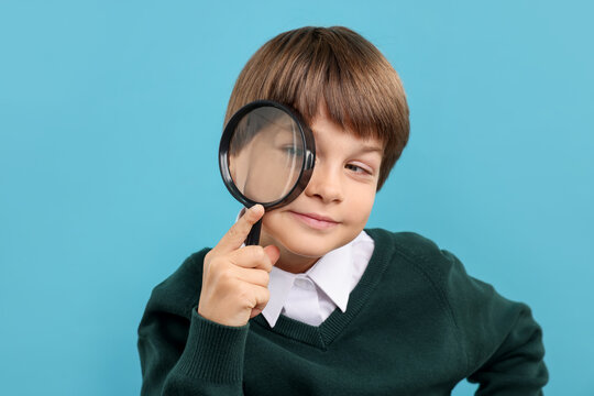 Little boy with magnifying glass on light blue background - Powered by Adobe