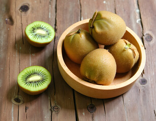 Fresh ripe kiwi fruits in a wooden bowl on a rustic table.
